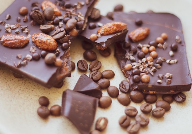 Chocolat noir haché avec amandes et grains de café. Chocolat cassé sur plaque beige. Aliments sucrés.