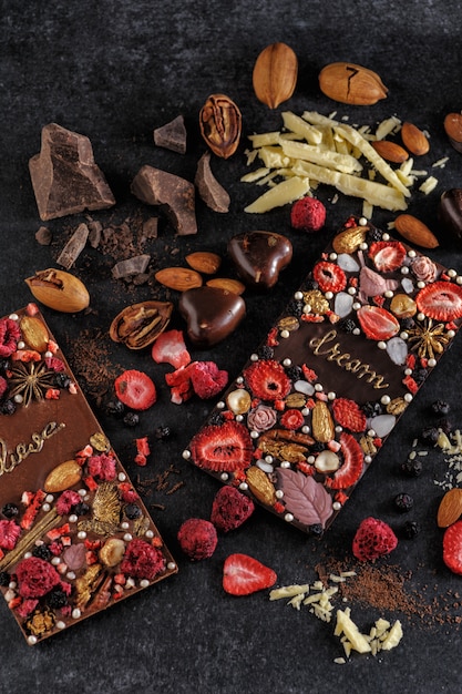 Chocolat noir et lait avec baies et noix lyophilisées à la main, naturel sur fond sombre