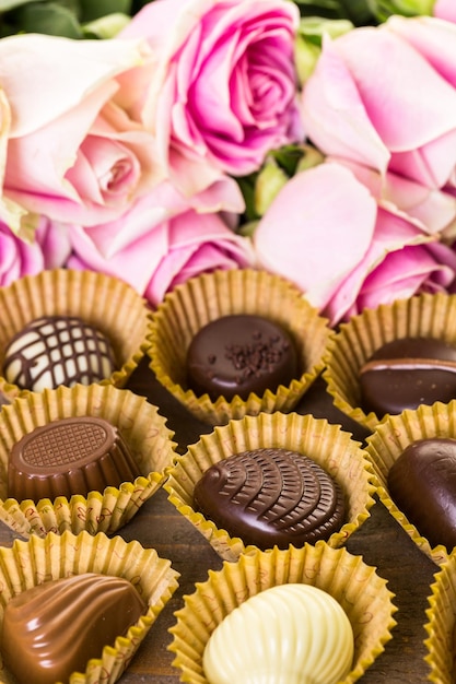 Chocolats assortis avec des roses roses sur table en bois.