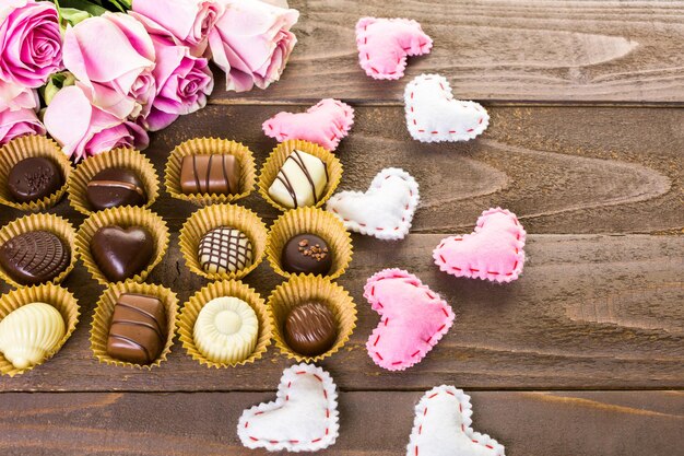 Chocolats assortis avec des roses roses sur table en bois.