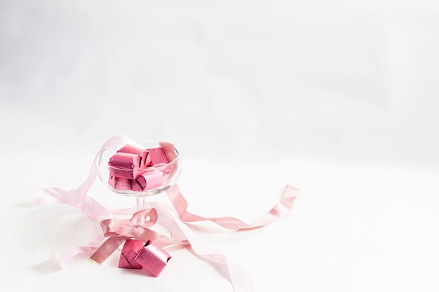 Chocolats avec du papier rose dans une tasse en verre avec des arcs roses sur fond blanc