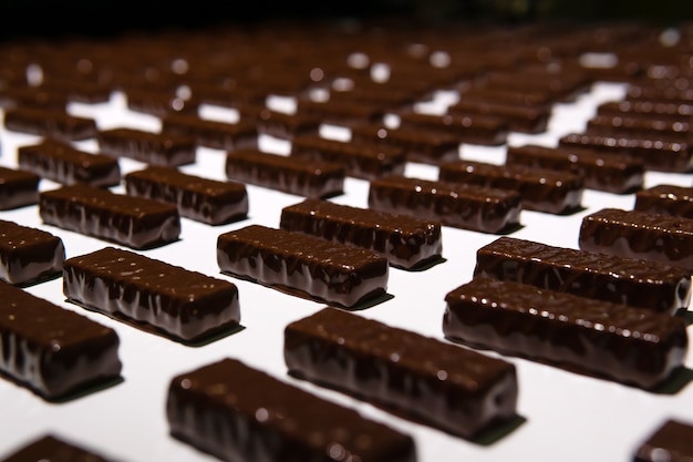 Chocolats juste versés avec du chocolat liquide sur un tapis roulant d'une usine de confiserie