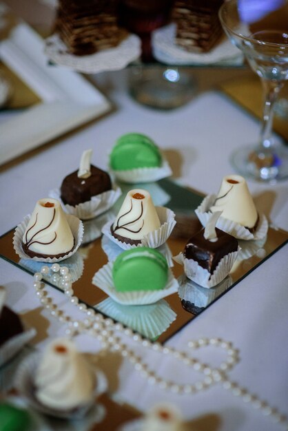 Des chocolats originaux et des macarons verts sur une plaque de miroir carrée