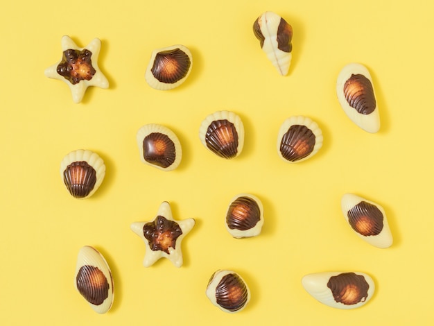 Chocolats sous forme de coquillages et coquillages sur un tableau jaune. La douceur du chocolat au lait. La vue du haut. Mise à plat.