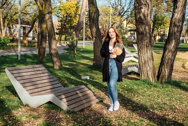 Choisir une étudiante universitaire avec des livres et un ordinateur portable à l'extérieur du collège rousse