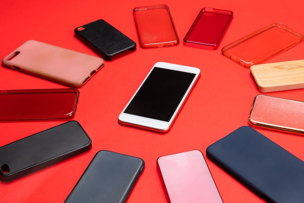 Photo choix de coques arrières en plastique multicolores pour téléphones portables sur fond rouge avec un smartphone sur le côté