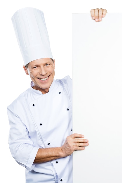 Choix du chef. Chef mûr confiant en uniforme blanc regardant hors de l'espace de copie et souriant en se tenant debout sur fond blanc