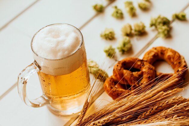 chope de bière, cônes de houblon, épillets de seigle et de blé et bretzels sur bois blanc