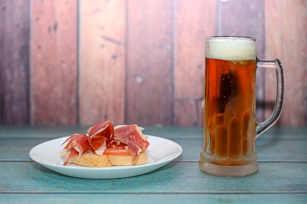 Chope de bière glacée avec un apéritif Jamon sur une table en bois