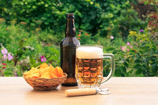 Chope en verre de bière et bouteille de bière sur une table en bois avec des croustilles dans un panier en osier et un ouvre-porte