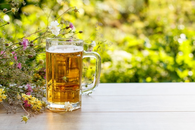 Chope en verre de bière sur table en bois avec bouquet de fleurs sauvages sur fond flou vert naturel