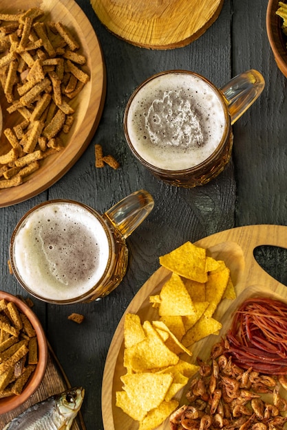 Chopes de bière froide avec de la mousse servies sur une table en bois avec des collations salées dans un bol en bois