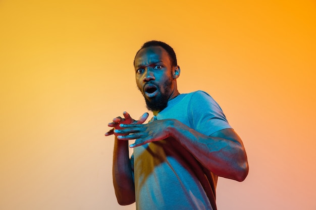 Choqué, effrayé. Portrait moderne de l'homme afro-américain sur fond de studio orange dégradé à la lumière du néon. Beau modèle afro. Concept d'émotions humaines, d'expression faciale, de ventes, d'annonces. Espace de copie.