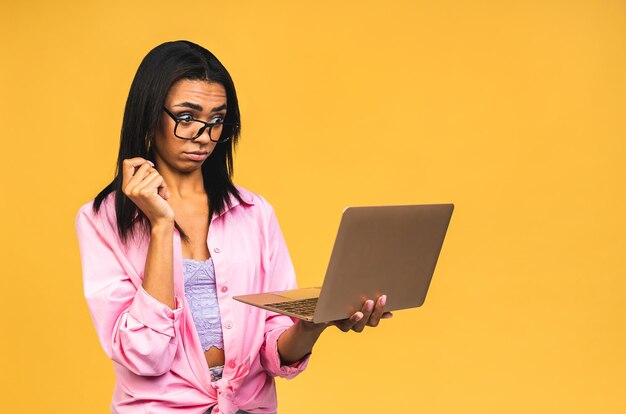 Choqué étonné afro-américain noir d'affaires ou étudiant femme posant isolé sur fond jaune Maquette copie espace Travail sur ordinateur portable pc