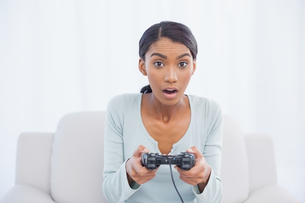 Choqué femme assise sur le canapé en jouant à des jeux vidéo