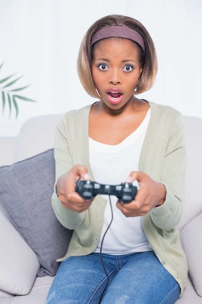 Choqué femme assise sur le canapé en jouant à des jeux vidéo