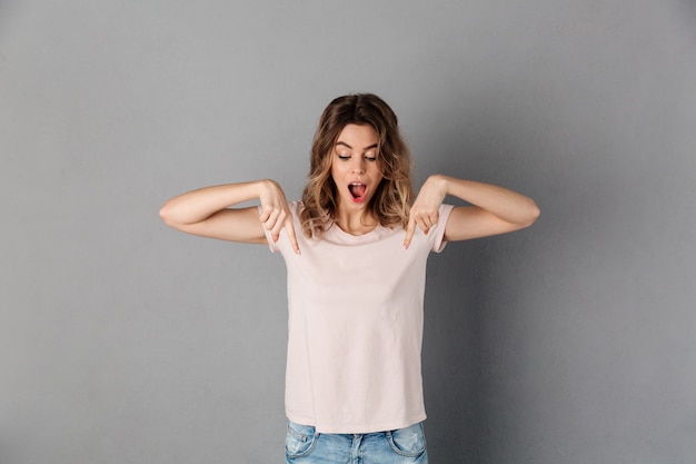 Choqué femme heureuse en t-shirt pointant et regardant vers le bas avec la bouche ouverte