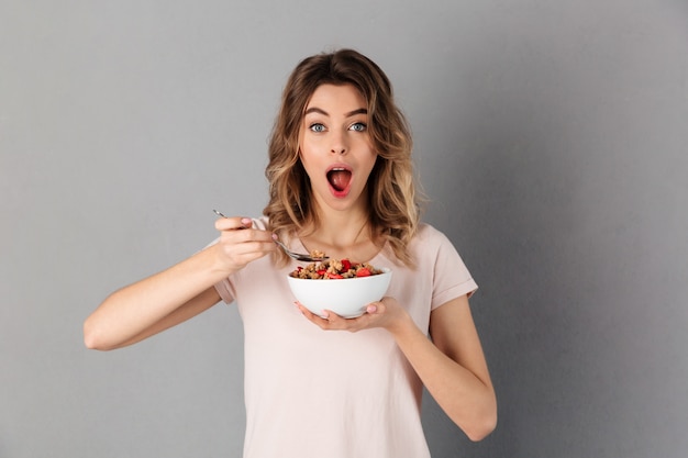 Choqué femme en t-shirt, manger des aliments sains de la plaque et plus gris