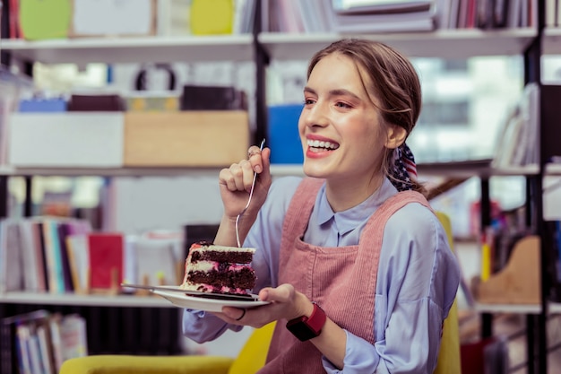 Choqué de goût. Rire fille attrayante séparant le morceau de gâteau avec une fourchette et désirant une bouchée