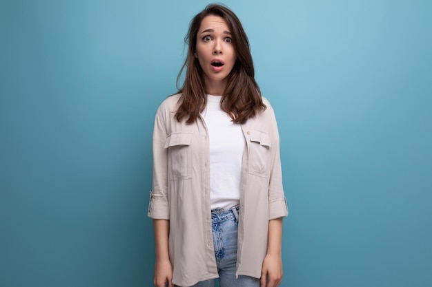 Choqué jeune femme brune en chemise et jeans avec la bouche ouverte