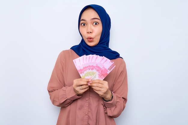 Choqué jeune femme musulmane asiatique en chemise rose tenant des billets de banque isolés sur fond blanc Les gens concept de style de vie religieux