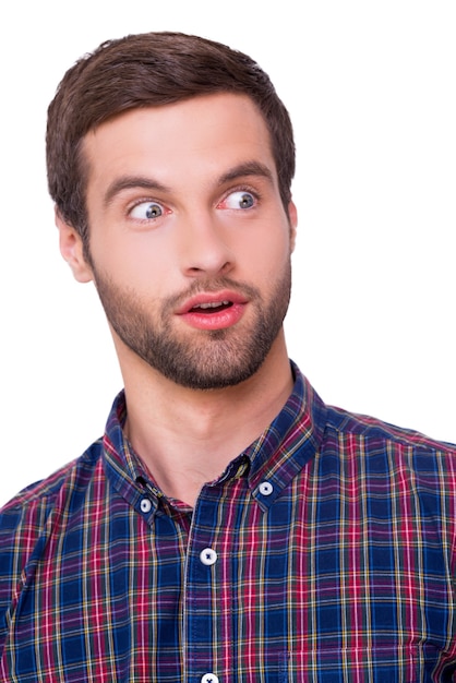 Choqué à propos de... Portrait d'un jeune homme choqué gardant la bouche ouverte tout en détournant les yeux tout en se tenant isolé sur blanc