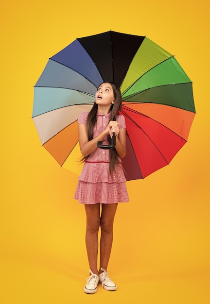 Choqué surpris adolescent fille robe d'été heureux adolescente tenant parapluie arc-en-ciel debout isolé sur fond jaune isolé sur blanc joyeux adolescent enfant tenir parasol