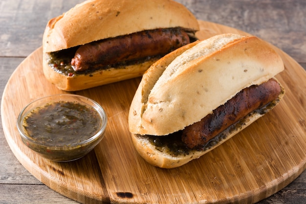 Choripan. Sandwich traditionnel de l'Argentine avec sauce chorizo et chimichurri sur une table en bois