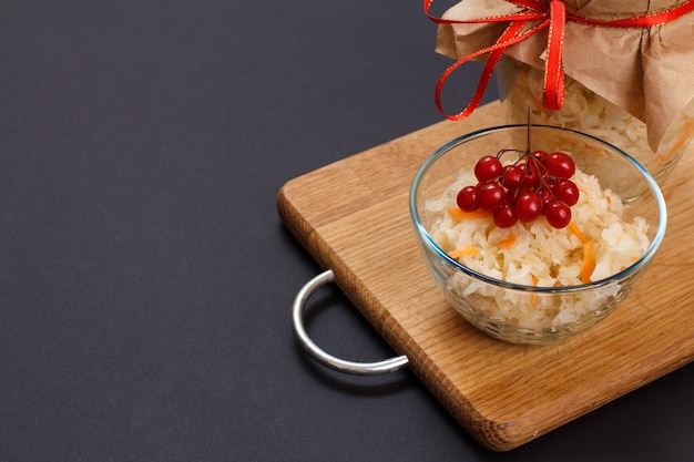 Chou fermenté fait maison avec carotte dans un bol en verre décoré d'une grappe de viorne et d'un bocal en verre sur l'arrière-plan. Salade végétalienne. Le plat est riche en vitamine U. Nourriture excellente pour une bonne santé.