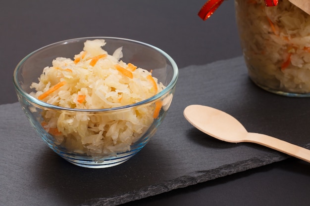 Chou Fermenté Maison Avec Carotte Dans Un Bol En Verre Et Peut Sur Fond Noir. Salade Végétalienne Dans Un Style Rustique. Le Plat Est Riche En Vitamine U. Aliments Excellents Pour Une Bonne Santé.