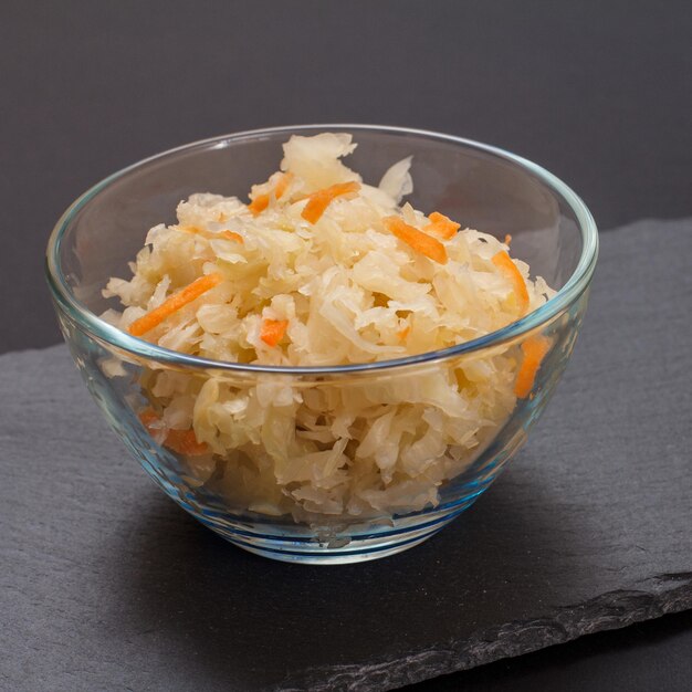 Chou fermenté maison avec carotte dans un bol en verre sur une planche en pierre noire. Salade végétalienne. Le plat est riche en vitamine U. Excellente nourriture pour une bonne santé.