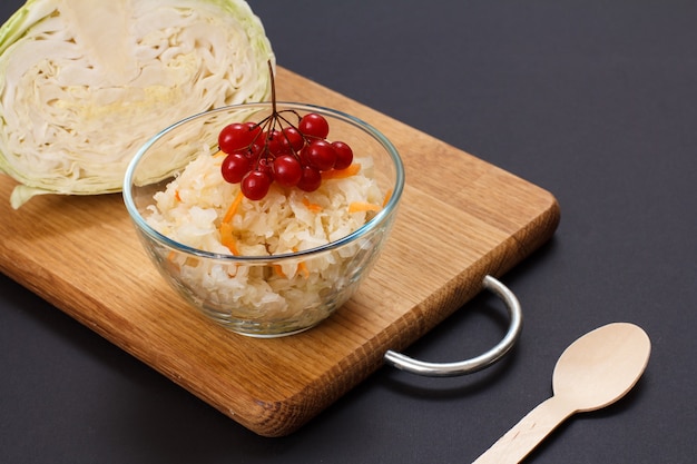 Chou fermenté maison avec carotte et grappe de viorne dans un bol en verre. Tête fraîche de chou sur le fond. Salade végétalienne. Le plat est riche en vitamine U. Nourriture excellente pour une bonne santé.