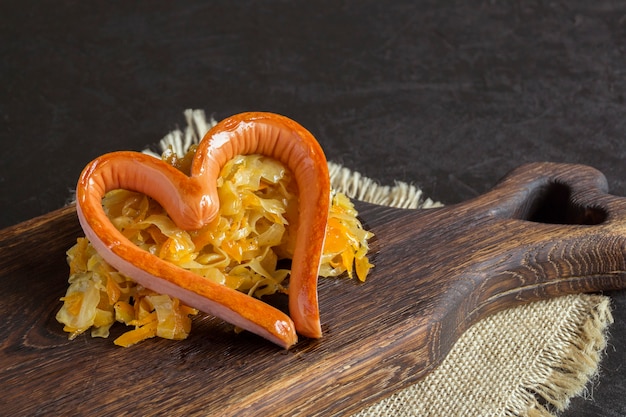 Photo chou mariné braisé avec saucisse grillée en forme de coeur. sur une planche de bois