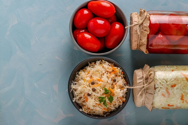 Choucroute maison et tomates salées dans des bols et des bocaux en verre sur fond bleu clair, Concept de légumes fermentés, vue de dessus