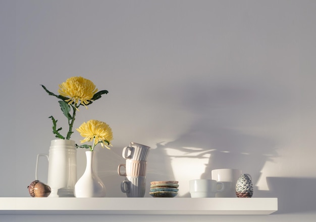 chrysanthème jaune dans un vase et des tasses sur une étagère blanche sur fond blanc