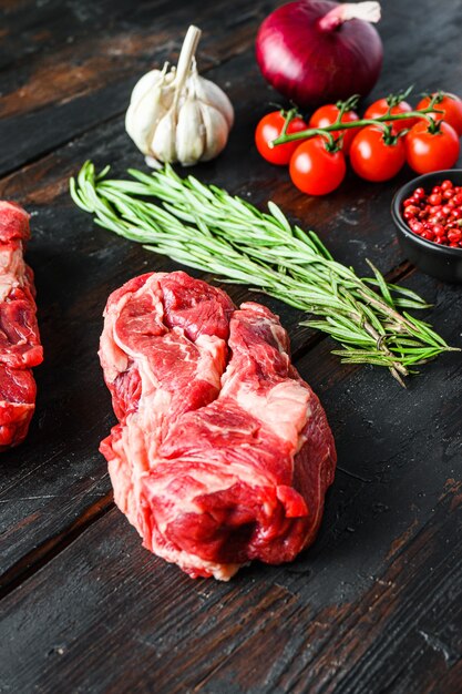 Photo chuck eye roll bifteck de boeuf cru coupé avec onin rouge romarin, grains de poivre à l'ail et tomates sur la vieille table en bois sombre. vue de côté.