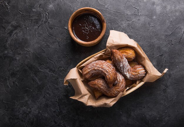 Churros dans un sac en papier avec du sucre et de la sauce au chocolat sur fond noir