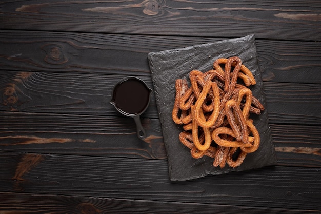 Churros faits maison avec du chocolat sur un fond rustique en bois foncé