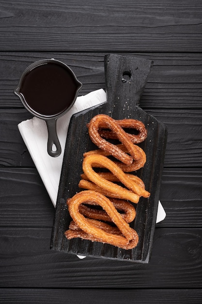 Churros faits maison avec du chocolat sur un fond rustique en bois foncé