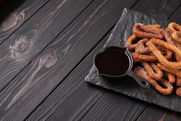 Churros faits maison avec du chocolat sur un fond rustique en bois foncé