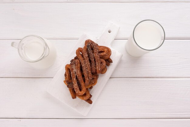 Churros faits maison avec du lait et de la crème sur un fond en bois blanc