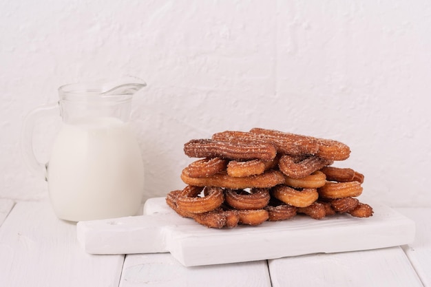 Churros faits maison avec du lait et de la crème sur un fond en bois blanc