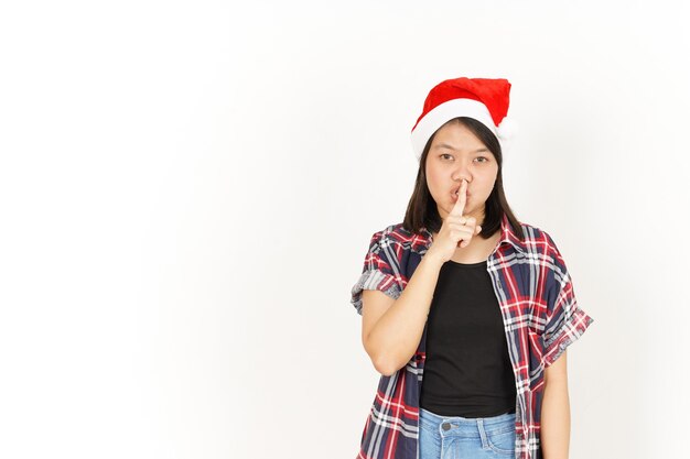 Chut tais-toi de la belle femme asiatique portant une chemise à carreaux rouge et un bonnet de noel isolé sur blanc