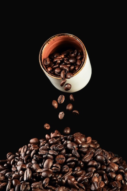 Chute de grains de café d'une tasse blanche et de grains de café fraîchement torréfiés sur le cadre vertical de la table sur fond noir