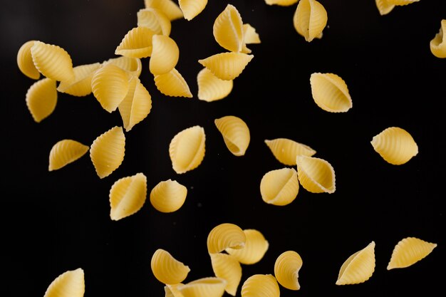 Chute de pâtes conchiglie. Macaroni cru jaune volant sur fond noir. DOF peu profond.