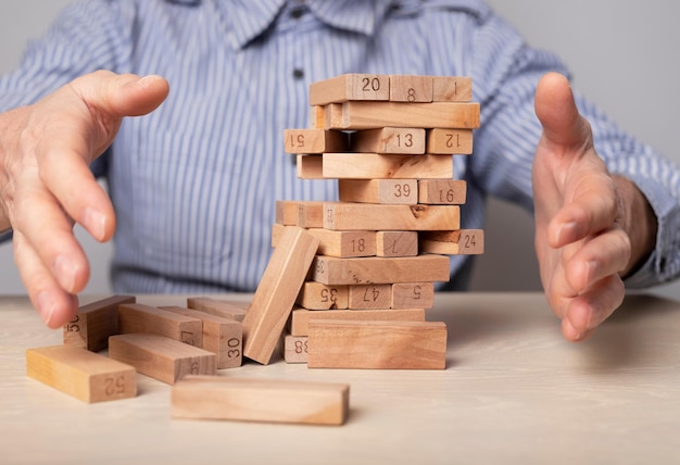 Chute de la tour de blocs de bois dans les mains d'un homme d'affaires en gros plan Crise économique et échec dans le concept d'entreprise Gestion des risques et planification stratégique