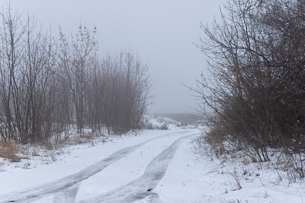 Chutes de neige sur la route d'hiver. Une route rurale vide sans voitures, couverte de congères. Voyager par mauvais temps