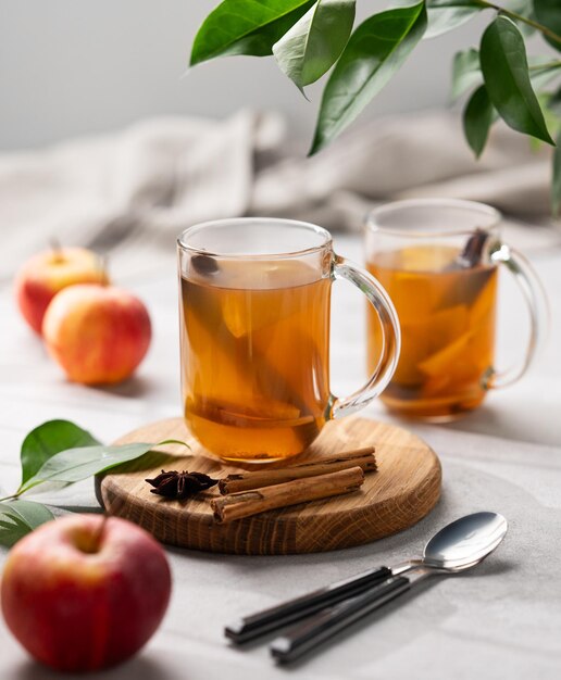 Cider de pomme fait maison avec des pommes et de la cannelle dans des tasses sur une planche de bois sur un fond clair avec des épices de fruits frais et une branche