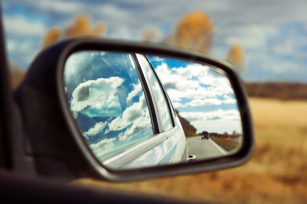 Ciel bleu avec nuages duveteux et reflet de la route un miroir de voiture sur fond de champ automne