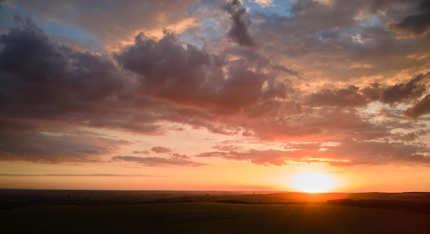 Un ciel coloré au coucher du soleil avec un soleil couchant et des nuages vibrants sur un paysage sombre